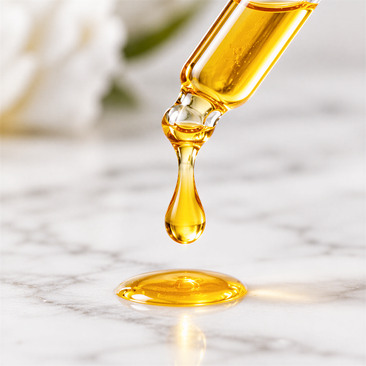 Golden serum dripping from a glass dropper onto a pale stone surface.